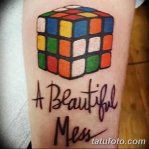 Фото тату: Кубик Рубика с надписью "A Beautiful Mess" на руке. Яркие цвета и каллиграфический шрифт создают интересный контраст.