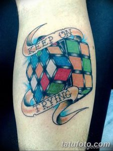 Фото тату кубика Рубика на предплечье с надписью 'KEEP ON TRYING'. Яркие цвета и динамичная композиция.
