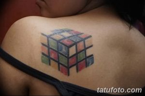 Фото тату кубика Рубика на плече. Минималистичный рисунок с использованием пастельных тонов.