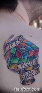 Фото татуировки кубика Рубика на груди с надписями "Life's a Puzzle, Grab It". Яркие цвета и классический стиль.