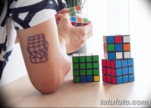 Фотография минималистичной татуировки на руке, изображающей контур кубика Рубика. Тату выполнено в простых линиях и ограниченной цветовой палитре.