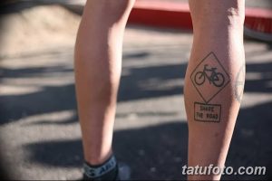 Фото тату велосипедного знака 'Share the Road' на икре. Черно-белый рисунок татуировки, минималистичный стиль, предупреждающий символ для велосипедистов.