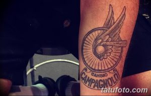 Фото тату велосипеда Campagnolo на руке. Черно-серый рисунок с логотипом и надписью, выполненный в реалистичном стиле.