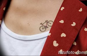 Фото тату на ключице: маленький контурный рисунок велосипеда, выполненный тонкими линиями черными чернилами.