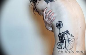 Фото тату на спине: стилизованный велосипед, растущий из одуванчика, выполненный в технике графики с использованием черных чернил.