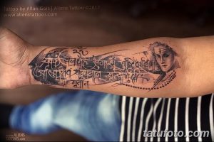 Фото тату на руке: изображение Шивы в окружении санскритских мантр, выполненное в реалистичном стиле с элементами акварели. Красивый и детализированный рисунок татуировки.