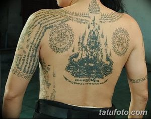 Фото татуировки, покрывающей всю спину. Изображены буддийские мандалы, символы и текст на древнем языке. Детализированный рисунок татуировки выполнен в серо-черных тонах.