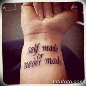 Фотография татуировки на запястье, представляющей собой фразу 'self made or never made', выполненную черными чернилами в каллиграфическом стиле.
