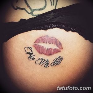 Фото тату на бедре с изображением красных губ и надписи 'Kiss Me All'. Чувственный и привлекательный рисунок татуировки.