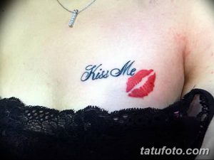 Фото тату с изображением красных губ и надписи 'Kiss Me' на груди девушки. Нежный и соблазнительный рисунок татуировки.