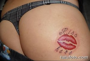 Фото тату: Отпечаток красных губ и надпись "Kiss here" на женских ягодицах. Провокационный и игривый рисунок татуировки.