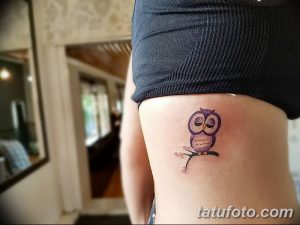 Маленькая фиолетовая татуировка совы, сидящей на ветке с цветущими вишневыми цветами. Тату расположена на боку.