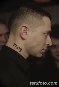 Черно-белое фото татуировки с цифрами '1703' на шее мужчины. Минималистичный дизайн, четкие линии, небольшая татуировка, расположенная сбоку шеи.