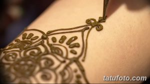 Фото процесса нанесения татуировки хной на кожу, с изображением тонкого узора и инструмента для нанесения хны.