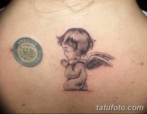 Фото миниатюрной татуировки ангела, склонившегося в молитве, на груди. Черно-серый рисунок, детализированные крылья, нежный стиль.