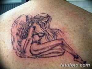 Фото тату ангела в сидячей позе на лопатке. Рисунок выполнен в черно-серых тонах, с акцентом на детализацию крыльев и волос.