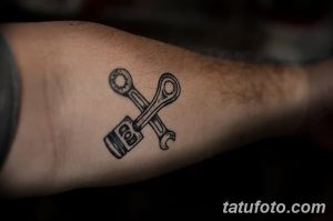 Фото тату на предплечье: перекрещенные ключ и поршень двигателя. Черно-белый рисунок, минималистичный дизайн, простая форма.