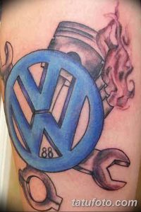 Фото тату с изображением логотипа Volkswagen и гаечного ключа, выполненное в ярких синих и красных тонах на предплечье.
