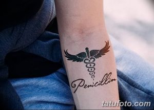 Небольшая черно-серая татуировка на предплечье с изображением символа Эскулапа и надписью "Penicillin". Минималистичный дизайн татуировки.
