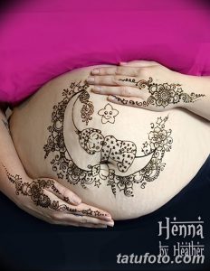 Фото тату Mehndi: сложный рисунок с полумесяцем, звездочками и растительными элементами, нанесенный на живот беременной женщины.
