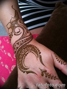 Фото тату Mehndi: сложный рисунок с полумесяцем, цветами и геометрическими узорами, нанесенный на запястье и руку.