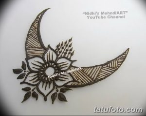 Фото тату Mehndi на руке: полумесяц, украшенный цветами и сложным орнаментом, выполненный в коричневых тонах.