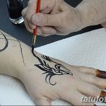 Фото процесса нанесения тату хной на руку, мастер аккуратно наносит узор с помощью кисти. Демонстрация техники и мастерства в искусстве мехенди.