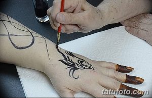 Фото процесса нанесения тату хной на руку, мастер аккуратно наносит узор с помощью кисти. Демонстрация техники и мастерства в искусстве мехенди.