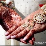 Фото тату мехенди на руках невесты, покрытых сложными узорами в красных тонах. Руки украшены браслетами и кольцами.