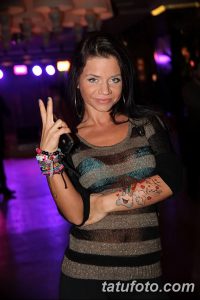 Фотография девушки, показывающей жест "V" и демонстрирующей татуировку на предплечье. Идеально для поиска идей для ярких и позитивных татуировок.