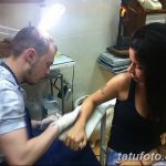 Фото процесса нанесения татуировки на руку девушки. Виден мастер тату и оборудование.
