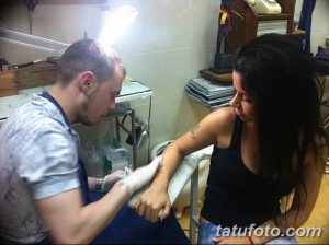 Фото процесса нанесения татуировки на руку девушки. Виден мастер тату и оборудование.