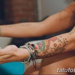 Фотография татуировки на руке, выполненной в стиле акварель. Изображены красочные облака, птицы, сердечки и надписи. Акварельная татуировка, рисунок татуировки.