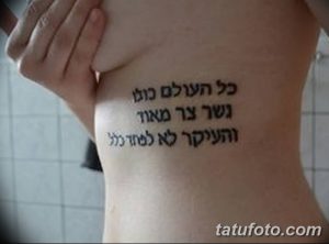 Фото татуировки с ивритской надписью, выполненной черными чернилами на боку женщины. Текст расположен вертикально вдоль ребер.