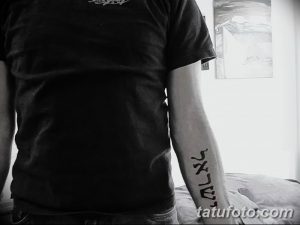Фото тату с ивритской надписью на предплечье. Черная татуировка с четкими линиями, выполненная в минималистичном стиле.