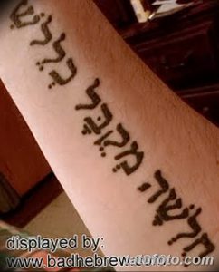 Фото тату: вертикальная надпись на иврите, выполненная черными чернилами на предплечье. Текст расположен вдоль руки, создавая элегантный и выразительный дизайн.