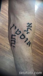 Фото татуировки с ивритской надписью, расположенной на голени. Черные чернила, оригинальный шрифт, динамичный дизайн.