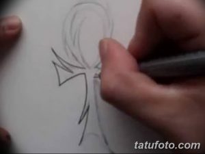 Фотография процесса создания эскиза татуировки с изображением египетского анкха. Рука мастера рисует контуры символа на бумаге.