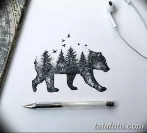 Фотография эскиза татуировки, изображающей силуэт медведя, внутри которого находится лесной пейзаж с деревьями и птицами. Рисунок выполнен в черно-белой графике.