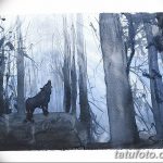 Фото тату: красивый акварельный эскиз татуировки с изображением волка, стоящего в зимнем лесу, выполненный в синих и серых тонах.