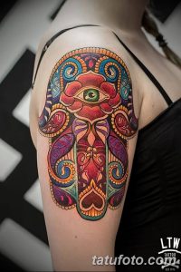 Фото цветной татуировки Хамсы на плече. Рука украшена яркими красками и сложным орнаментом, в центре расположен глаз.