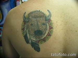 Классическая татуировка головы бизона в круге, украшенная перьями и этническими узорами. Изображение выполнено в ярких цветах и с четкими контурами.