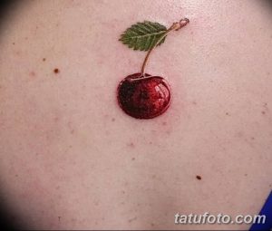 Фото минималистичной татуировки с изображением одной спелой вишни с зеленым листиком. Татуировка выполнена в реалистичном стиле на коже.