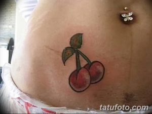 Фото тату вишни с листьями на животе. Небольшой и изящный рисунок татуировки, выполненный в ярких цветах.
