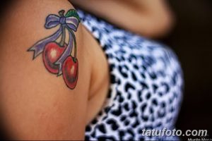 Фото тату вишни с фиолетовым бантом на плече. Женственный и яркий рисунок, выполненный в реалистичной технике. Идеальный эскиз для девушек.