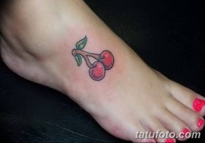 Фото маленькой татуировки вишни на стопе. Красные ягоды и зеленый лист создают простой, но привлекательный эскиз.