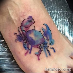 Фото акварельной татуировки краба на стопе. Нежный и красочный рисунок татуировки, выполненный в технике акварели с использованием синих и фиолетовых оттенков.