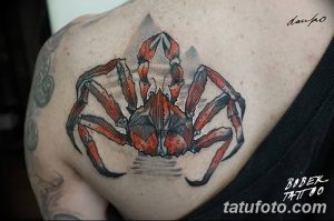 Фото реалистичной татуировки краба на плече. Краб с детально прорисованными клешнями и панцирем. Использование серых и красных оттенков.