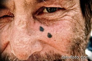 Фото тату двух маленьких черных точек, имитирующих родинки, на лице пожилого мужчины. Татуировки выполнены в реалистичном стиле.