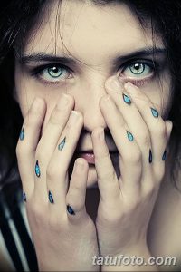 Фото тату: девушка закрывает лицо руками, на которых и на щеках изображены маленькие черные татуировки в виде капель. Выразительная и символичная татуировка.